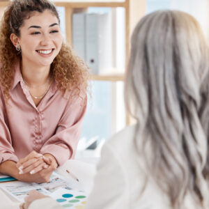 Two happy caucasian businesswomen having a meeting at a table in an office at work. Female business