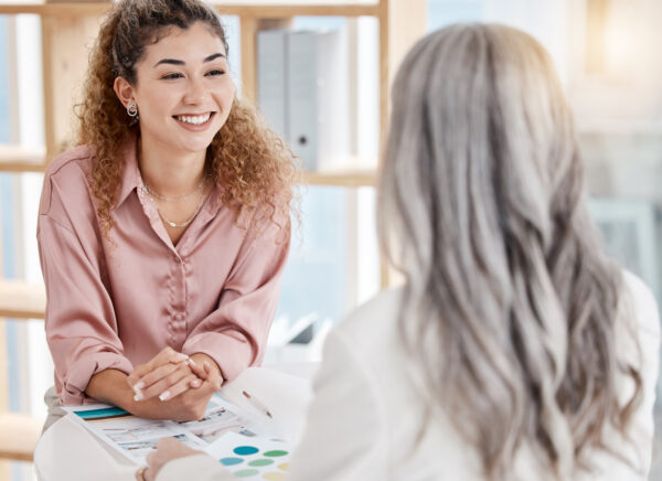 Two happy caucasian businesswomen having a meeting at a table in an office at work. Female business