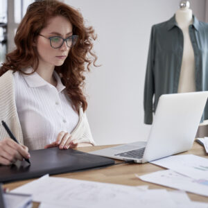 Young adult woman using laptop and designing a dress